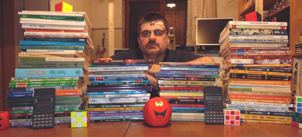 Mladen Sraga za stolom okružen zbirkama i udžbenicima matematike